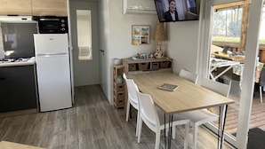 A modern kitchen with a microwave, oven, and refrigerator. There is a dining area with a table and chairs, and a television mounted on the wall. - Mobile Home 'Mobil Home Arès' in Arès, Near the Beach and Arcachon Bay (Arès)