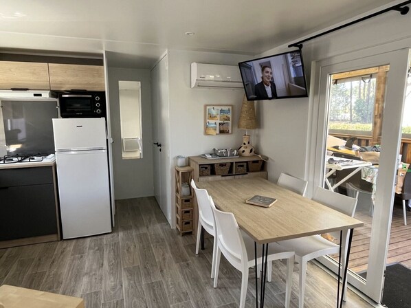 A modern kitchen with a microwave, oven, and refrigerator. There is a dining area with a table and chairs, and a television mounted on the wall.
