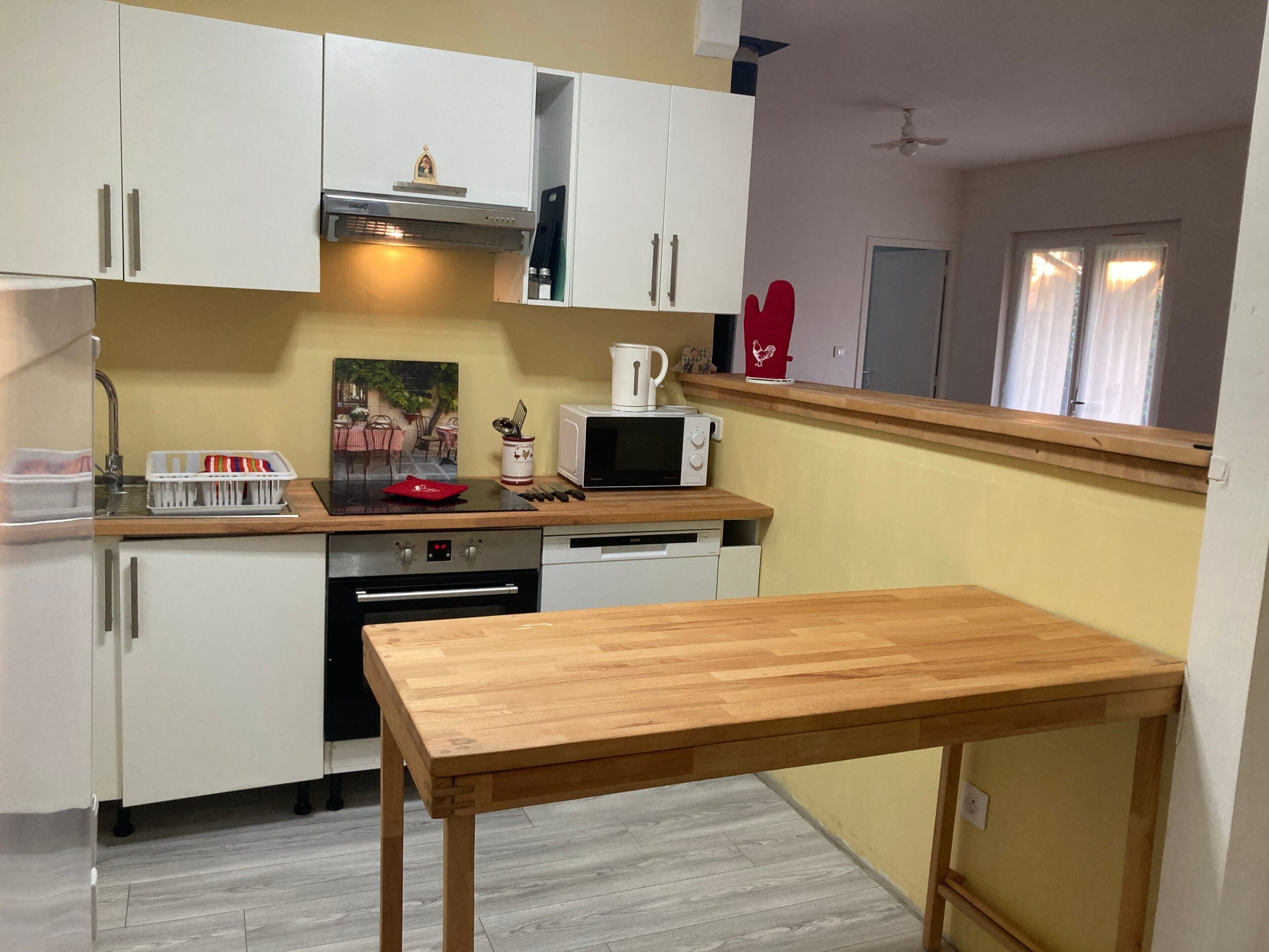 A compact kitchen with white cabinets, a microwave, a coffee maker, and a wooden table.