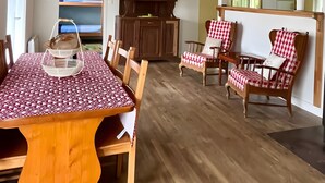 Un coin repas avec une table et des chaises en bois, un meuble avec des portes en verre, et une vue sur une pièce comprenant un lit et une fenêtre.