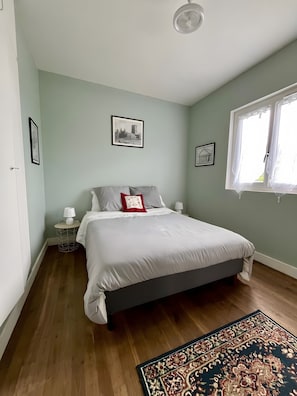 A bedroom with a bed, a nightstand, a lamp, a window with curtains, and a patterned rug.