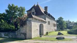 A stone building with a pitched roof, an arched entrance, and a small garden with rocks and grass. - Quercy Room – Romantic & Authentic Retreat (Gramat)
