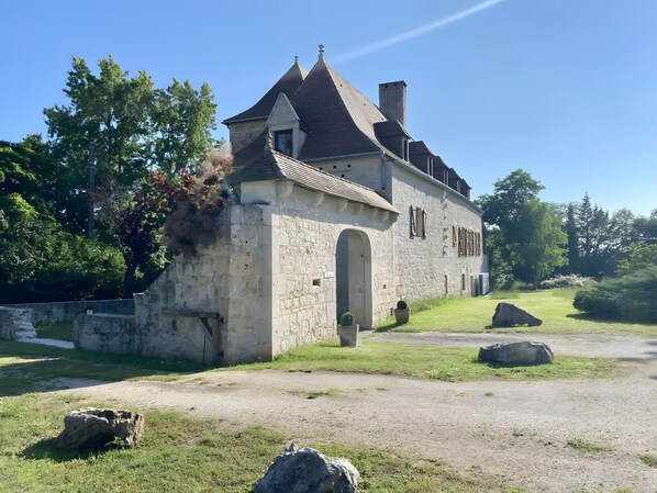 Ein Steinhaus mit Satteldach, einem Bogenportal und einem kleinen Garten mit Steinen und Gras.
