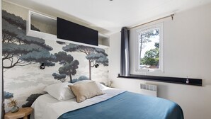 A bedroom with a bed, a window, a wall-mounted TV, and a mural. - Bungalow "Les Lodges Des Pins" with Shared Pool (Lège-Cap-Ferret)