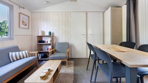 A modern living room with a sofa, a coffee table, a dining table with chairs, a bookshelf, and a wardrobe. - Bungalow "Les Lodges Des Pins" with Shared Pool (Lège-Cap-Ferret)