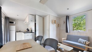 Een compacte leefruimte met kitchenette, eethoek, bank en raam met uitzicht op groen.