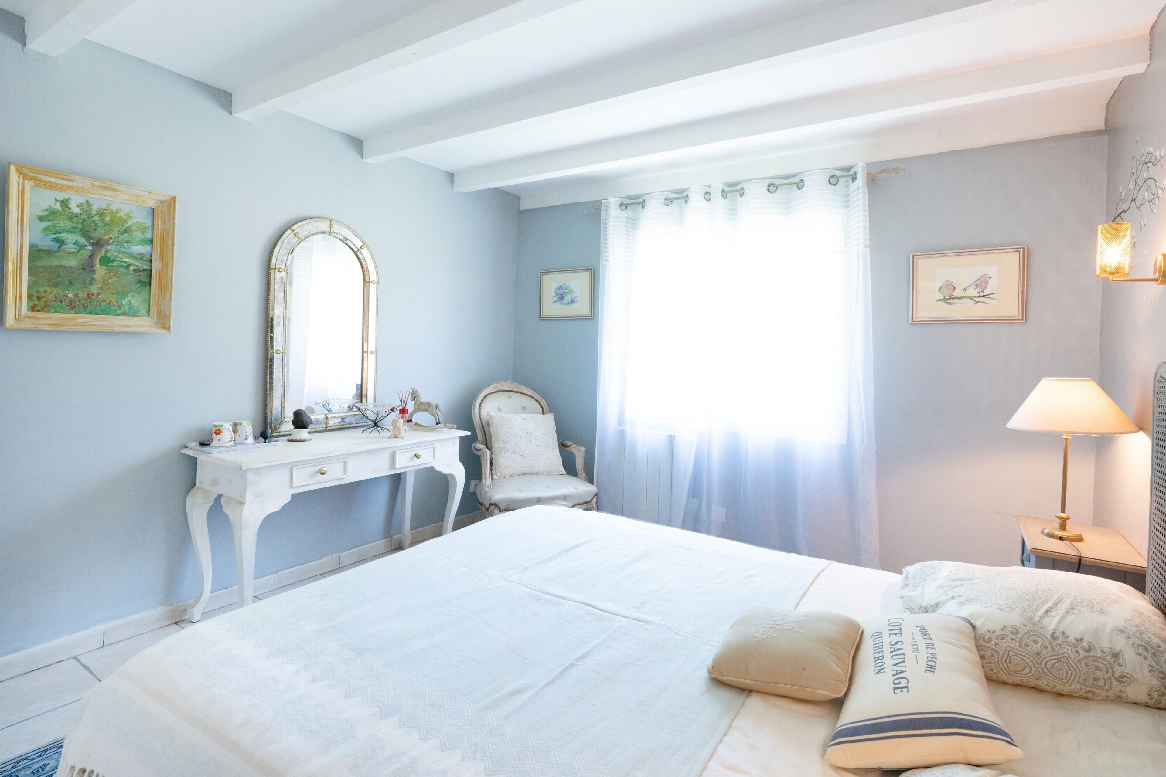 Un dormitorio con cama, cómoda, silla, espejo y ventana con cortinas.
