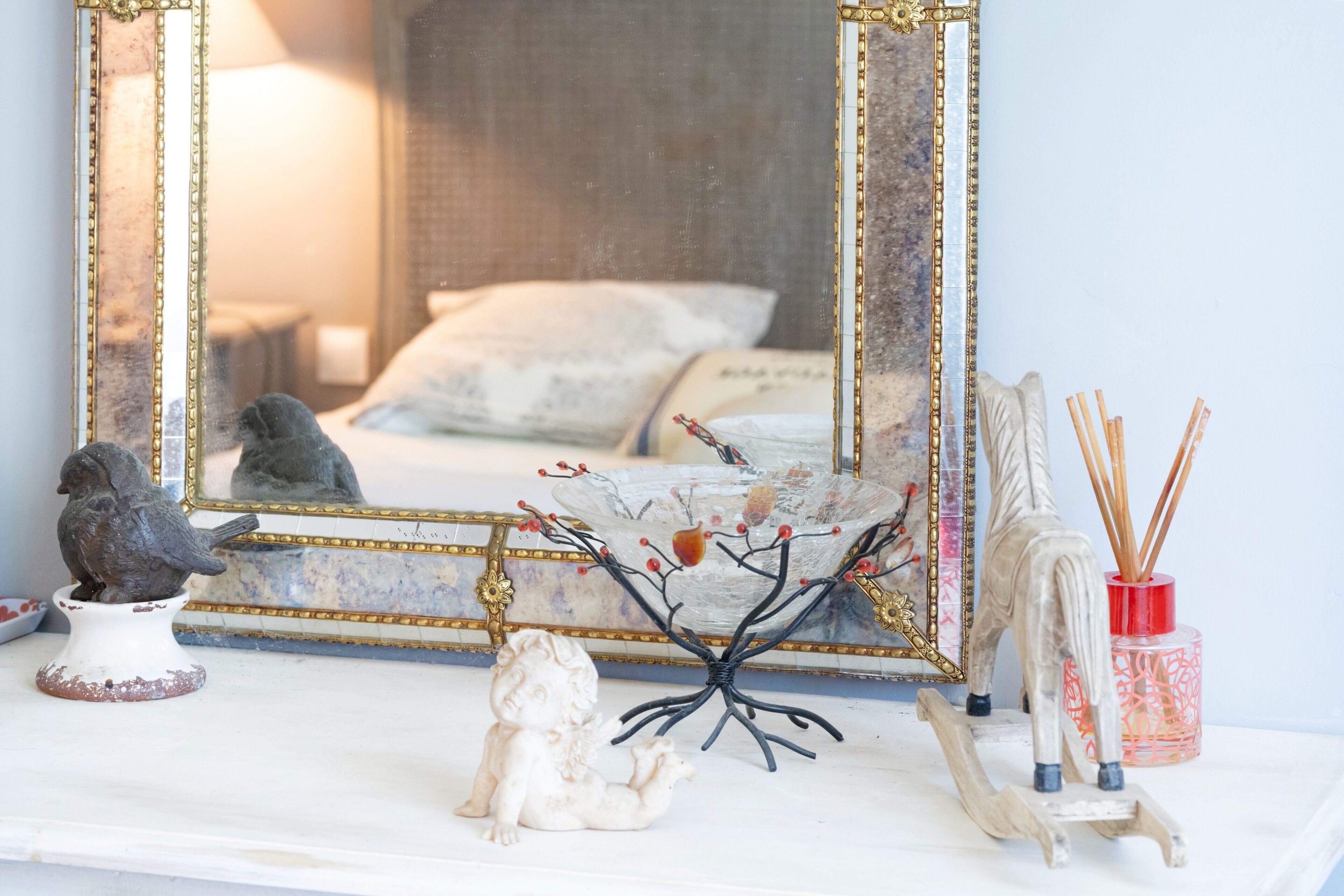 Une chambre à coucher comprenant un lit, une commode, un miroir et des objets décoratifs, notamment une sculpture d’arbre et une statuette d’oiseau.
