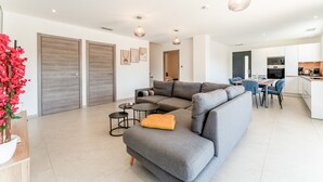 A modern living room with a grey sectional sofa, a small coffee table, and a dining area with blue chairs. - Modern Villa with Pool, Wi-Fi, and Air Conditioning (Beaucaire)