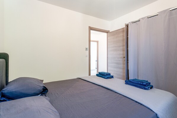 A bedroom with a bed, pillows, a blue towel, and a door leading to another room.