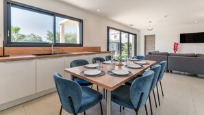 A modern dining area with a large table, blue chairs, and a kitchen counter. - Modern Villa with Pool, Wi-Fi, and Air Conditioning (Beaucaire)