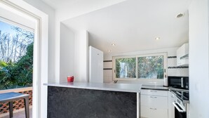 Une cuisine moderne avec des meubles blancs, un plan de travail noir et une fenêtre donnant sur un espace verdoyant.