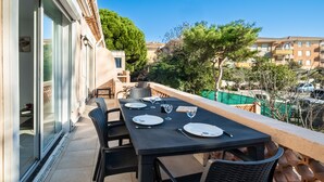 Un balcon avec une table dressée pour le dîner, des chaises et une vue sur les bâtiments et les arbres environnants.