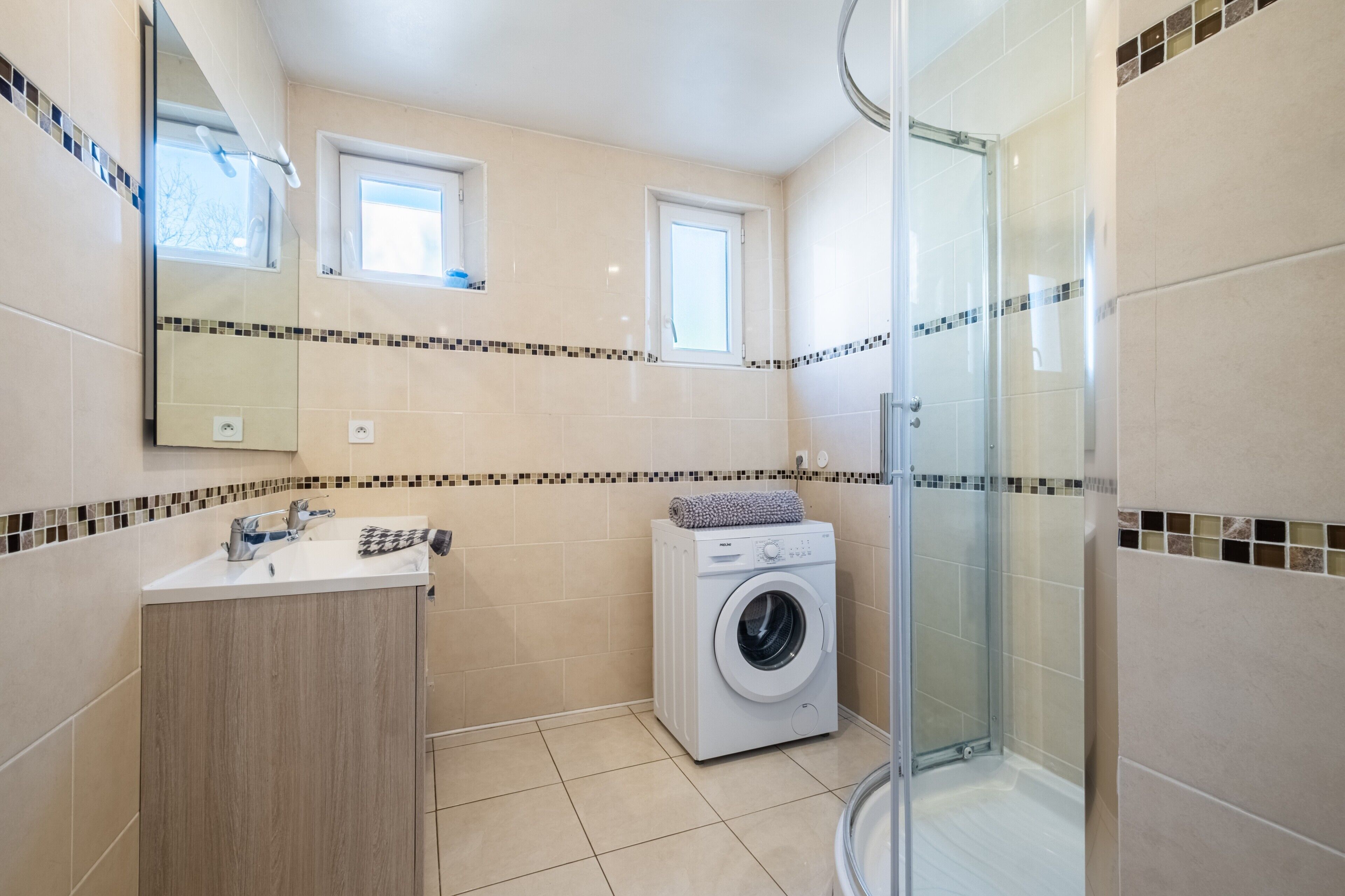 A bathroom with a washing machine, a sink, a mirror, and a shower.