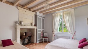 Een slaapkamer met een bed, een stoel, een tafel en een open haard.