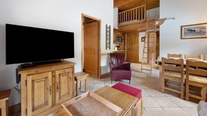 Amplia sala de estar con un televisor de pantalla plana grande, muebles de madera, una mesa de comedor y un entrepiso con una escalera de madera.