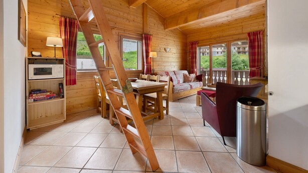 Interior de una cabaña de madera con comedor, sofá, escalera y un bote de basura.