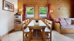 Un interior de madera con una mesa de comedor, sillas, un sofá, un televisor y una ventana con cortinas.