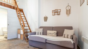 Ein Wohnzimmer mit einer Couch, einer Holzleiter, einer weißen Tür und einer Wand mit gerahmten Bildern und einem Traumfänger.