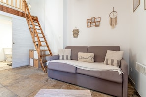 Un salon avec un canapĂ©, une Ă©chelle en bois, une porte blanche et un mur ornĂ© de tableaux et dâun attrape-rĂȘves.