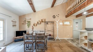 Ein geräumiges Zimmer mit Esstisch, Stühlen, einem Fernseher und einer Holztreppe.