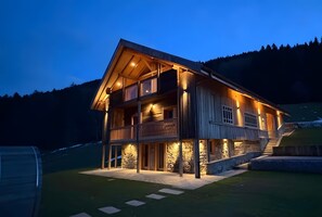 Une maison en bois à deux étages, dotée d’un balcon, de fondations en pierre et d’une allée menant à l’entrée.
