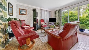 Una sala de estar con sillones de cuero rojo, un televisor y vistas al exterior con follaje.