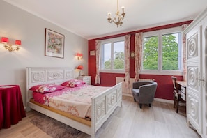 Ein Schlafzimmer mit Bett, Stuhl, Schreibtisch, Heizkörper und einem Fenster mit Vorhängen.