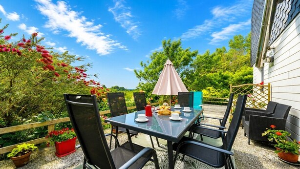 Un patio al aire libre con mesa y sillas, un paraguas rosa y plantas en macetas.