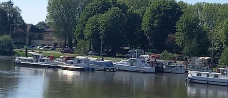 Une rivière paisible où plusieurs bateaux sont amarrés le long de la rive, entourée d’arbres et de bâtiments.