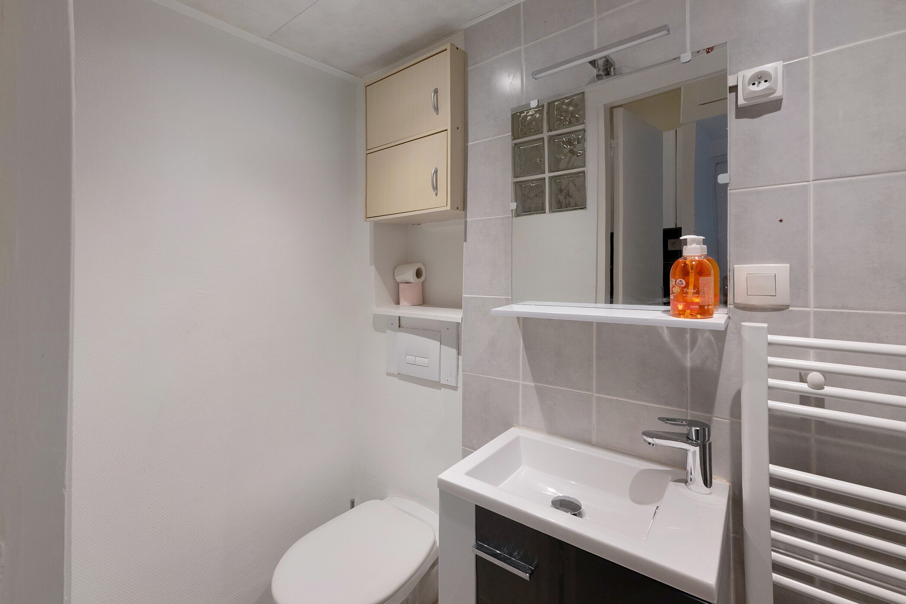 Une salle de bain moderne équipée de toilettes, d’un lavabo, d’un miroir et d’une étagère où sont rangés les articles de toilette.