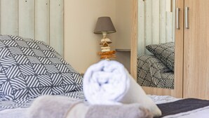 Een bed met beddengoed met patroon, een lamp met een uniek ontwerp en een houten garderobe met handgrepen.