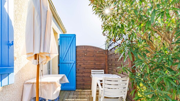 Een terras met een tafel en stoelen, een blauwe deur en een houten omheining.
