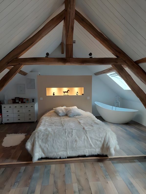 Ein Schlafzimmer im Dachgeschoss mit schräger Decke, einem großen Bett, einer Badewanne und einem an der Wand befestigten Regal mit Dekoration.