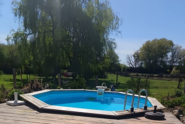 Een buitenzwembad met houten terras, omringd door bomen en een gazon.