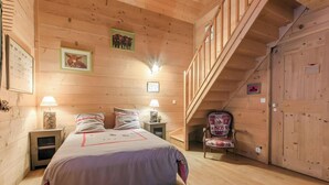 Une chambre à coucher dans une cabane en bois, avec un lit, deux lampes de chevet, une chaise et un escalier.