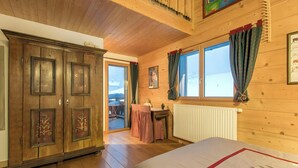L’intérieur d’un chalet en bois comprend une grande armoire, un lit, une table avec une chaise et une fenêtre avec des rideaux.