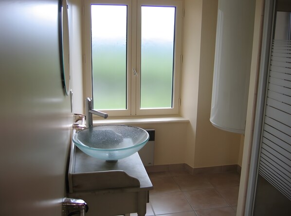 Un baño con lavamanos de vidrio, una ventana y una puerta.