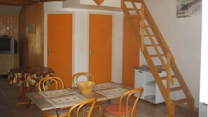 Ein Zimmer mit einer Holztreppe, einem Esstisch mit Stühlen, einem Fernseher und einem Poster an der Wand.