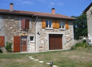 Un edificio de piedra con tejado de baldosas, contraventanas de madera y un amplio portón de garaje.