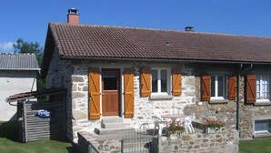 Ein Steinhaus mit Ziegeldach, Holzläden und einer kleinen Veranda mit Sitzgelegenheiten.
