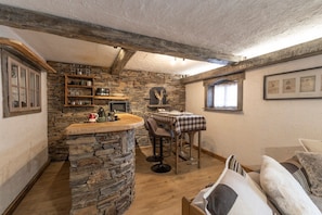 A rustic interior with a stone bar, wooden shelves, a checkered table, and a cozy seating area. - Apartment in Authentic Chalet with Mountain View, Shared Pool & Wi-Fi (Les Contamines-Montjoie)