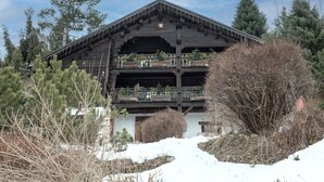 Una cabaña de madera con varios balcones, rodeada de nieve y árboles.