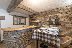 A rustic kitchen with stone walls, a wooden counter, and a checkered tablecloth. - Apartment in Authentic Chalet with Mountain View, Shared Pool & Wi-Fi (Les Contamines-Montjoie)