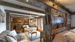 Un interior rústico con vigas de madera a la vista, una chimenea de piedra y una zona de estar acogedora con un sofá y una mesita de centro.