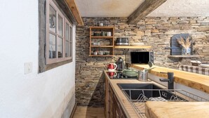 Una cocina con pared de piedra, estantes de madera, un microondas y un lavamanos.