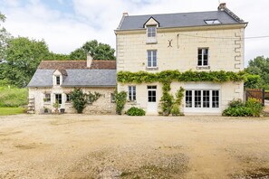 A two-story stone house with a gravel driveway, a small attached structure, and a garden area. - Bed and Breakfast 'Les Prés Hauts' with Shared Garden and Wi-Fi (Rigny Ussé)