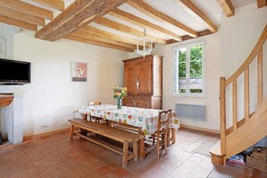 Un espace repas comprenant une table en bois, des bancs, un lustre, un buffet en bois et un téléviseur.