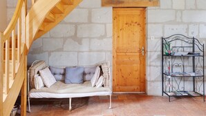 Una habitación con escalera de madera, un sofá acolchado, una puerta de madera y una estantería metálica con objetos.