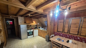 Cocina rústica con vigas de madera, refrigerador, estufa, microondas y comedor con mesa y sillas.